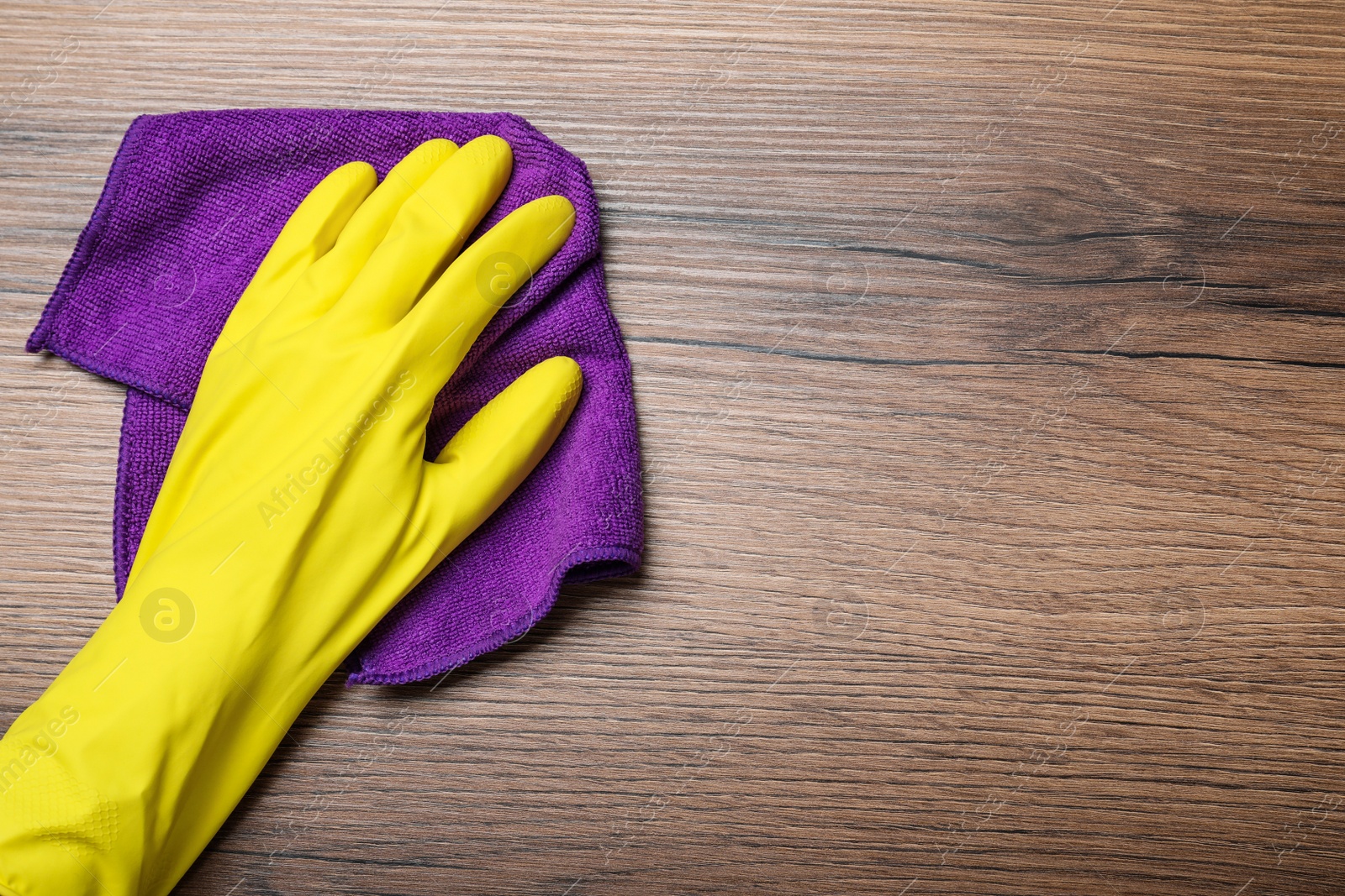 Photo of Woman in yellow rubber gloves wiping wooden table with microfiber cloth, top view. Space for text