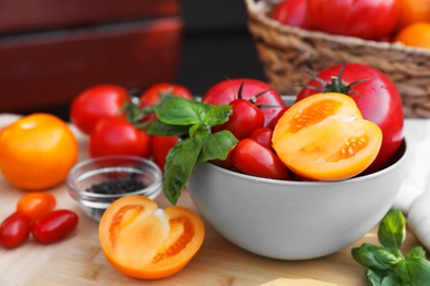 Different sorts of tomatoes with basil on wooden table