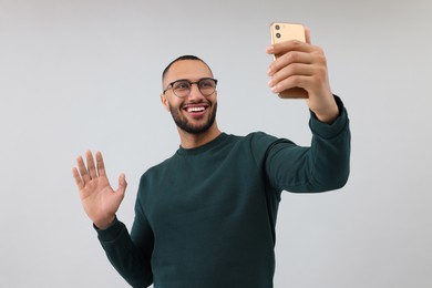 Smiling young man taking selfie with smartphone on grey background