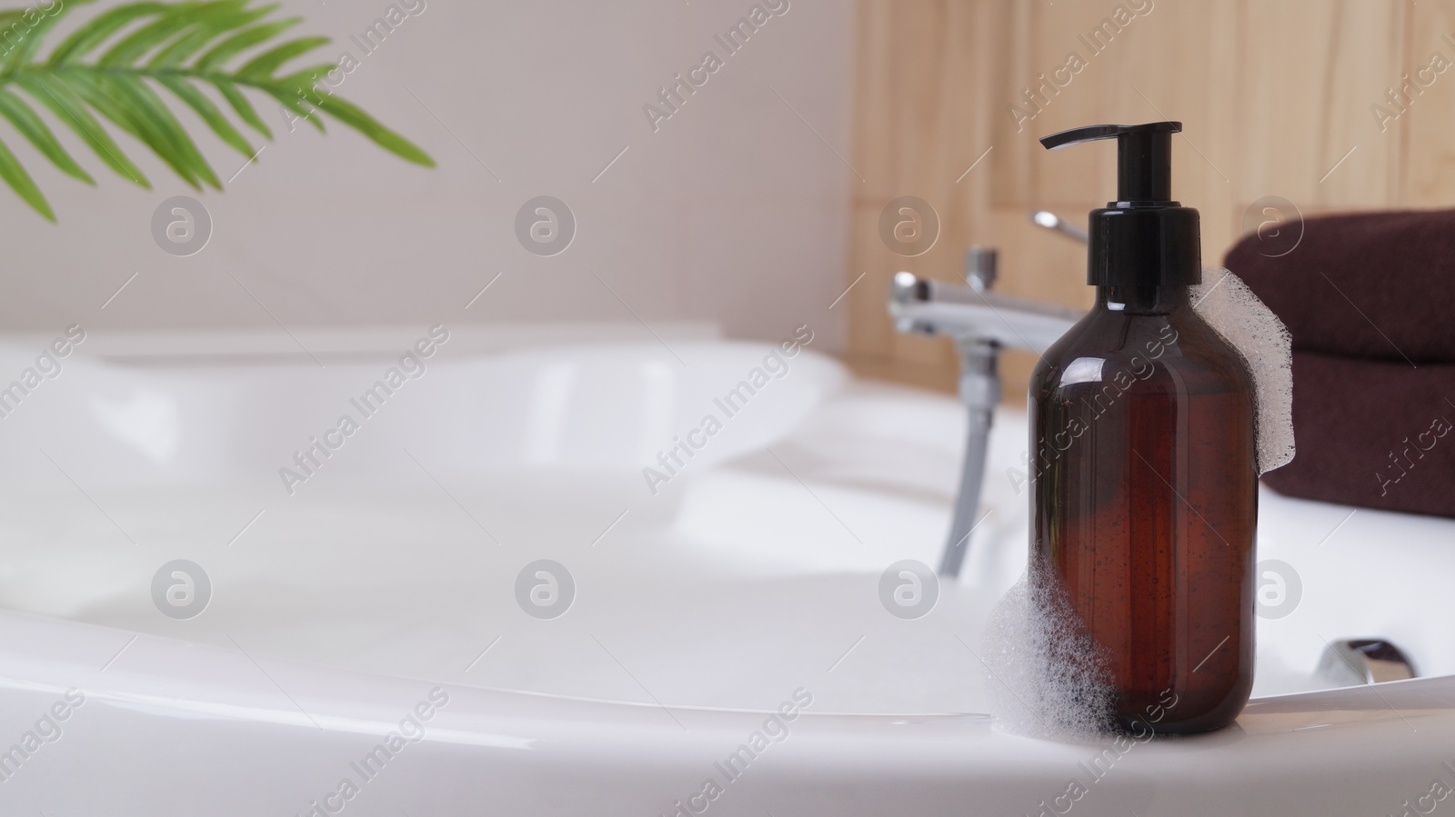 Bottle of bubble bath with foam on tub indoors, space for text Photo of Bottle of bubble bath with foam on tub indoors, space for text