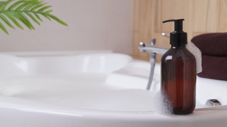 Photo of Bottle of bubble bath with foam on tub indoors, space for text