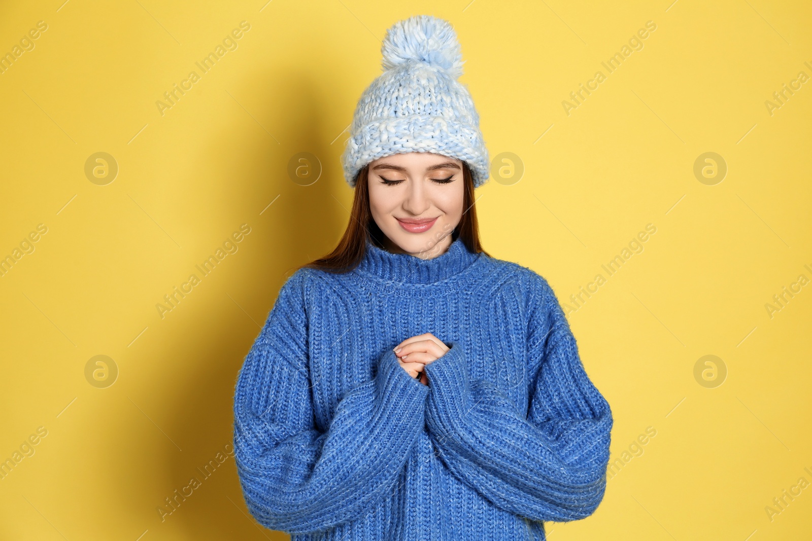 Photo of Young woman wearing warm sweater and hat on yellow background. Winter season