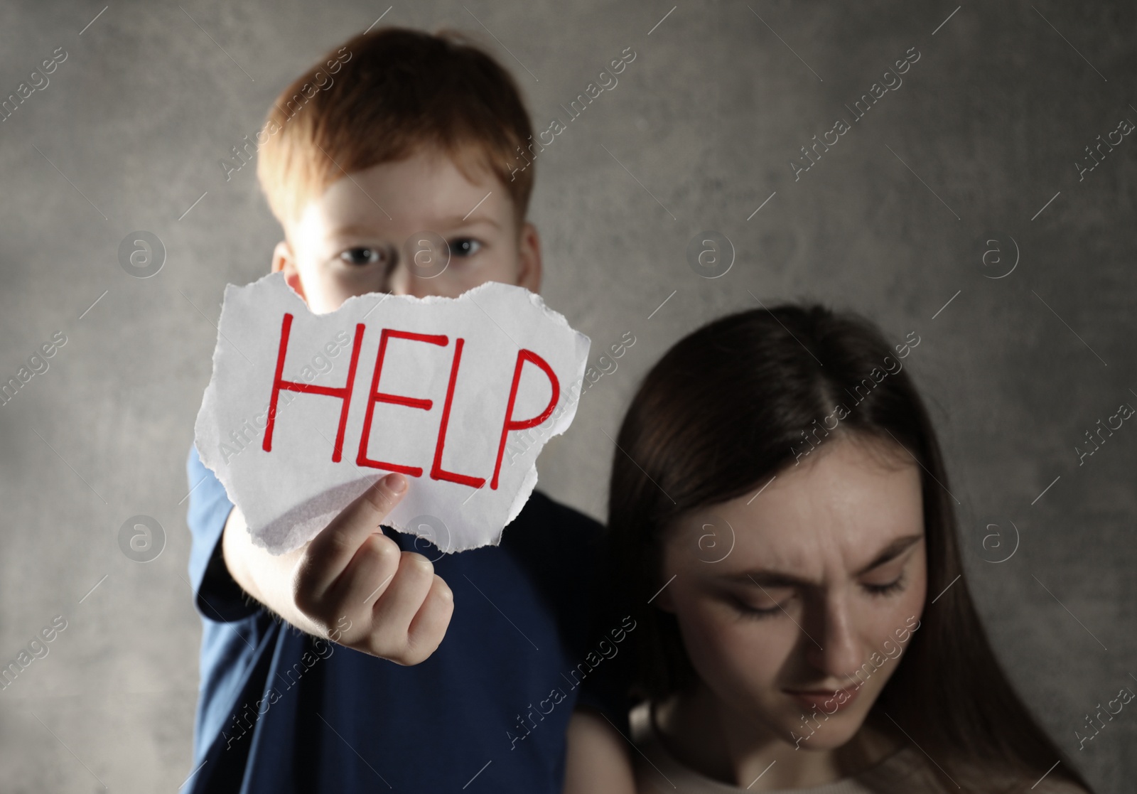 Photo of Scared mother and little boy holding piece of paper with word Help against light grey background. Domestic violence concept
