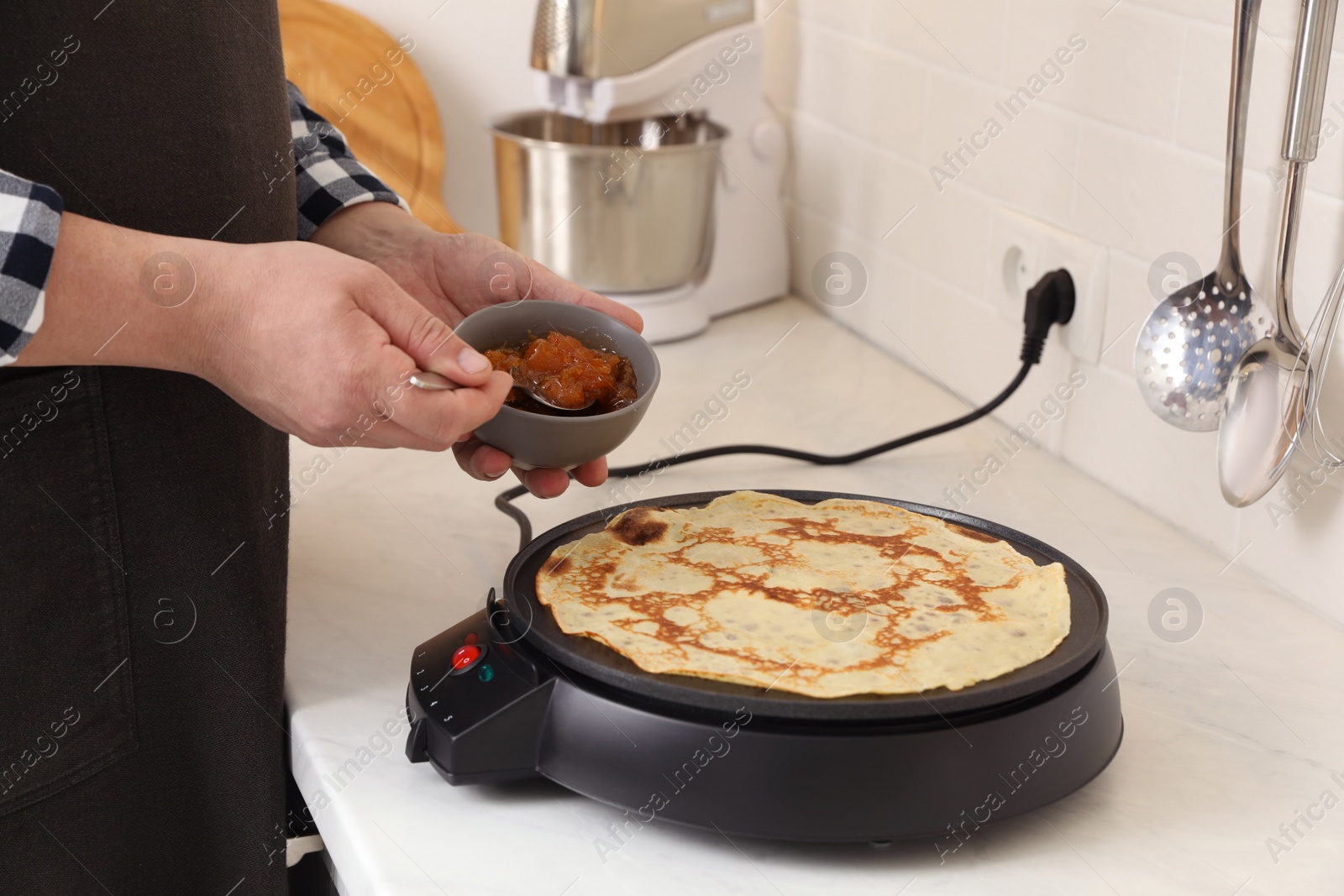 Photo of Man cooking delicious crepe on electric pancake maker in kitchen, closeup