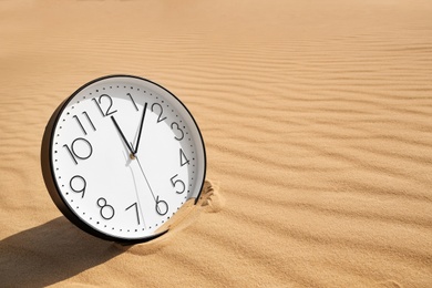 Photo of Stylish clock on sand in desert. Space for text