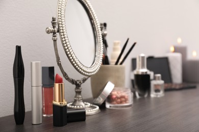 Photo of Mirror, candles and different makeup products on dark wooden dressing table near wall