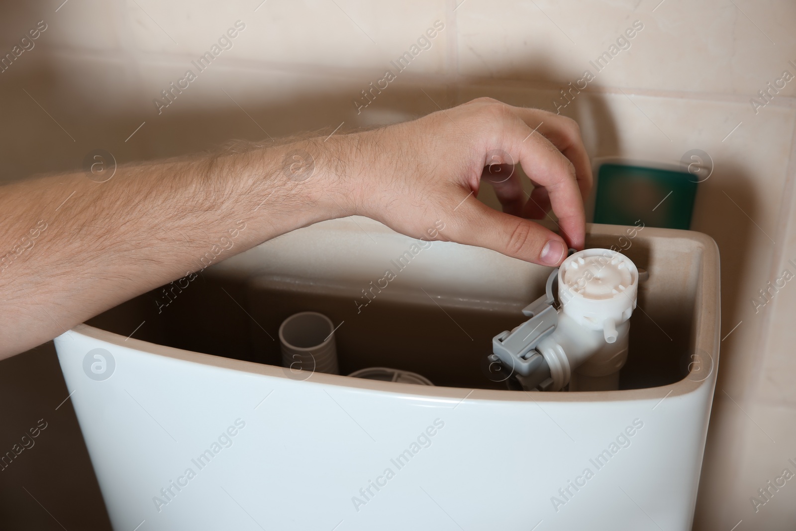 Photo of Professional plumber repairing toilet tank indoors, closeup