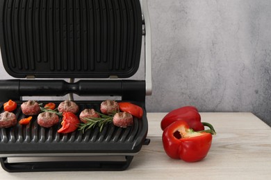 Photo of Electric grill with vegetables, meat balls and rosemary on wooden table