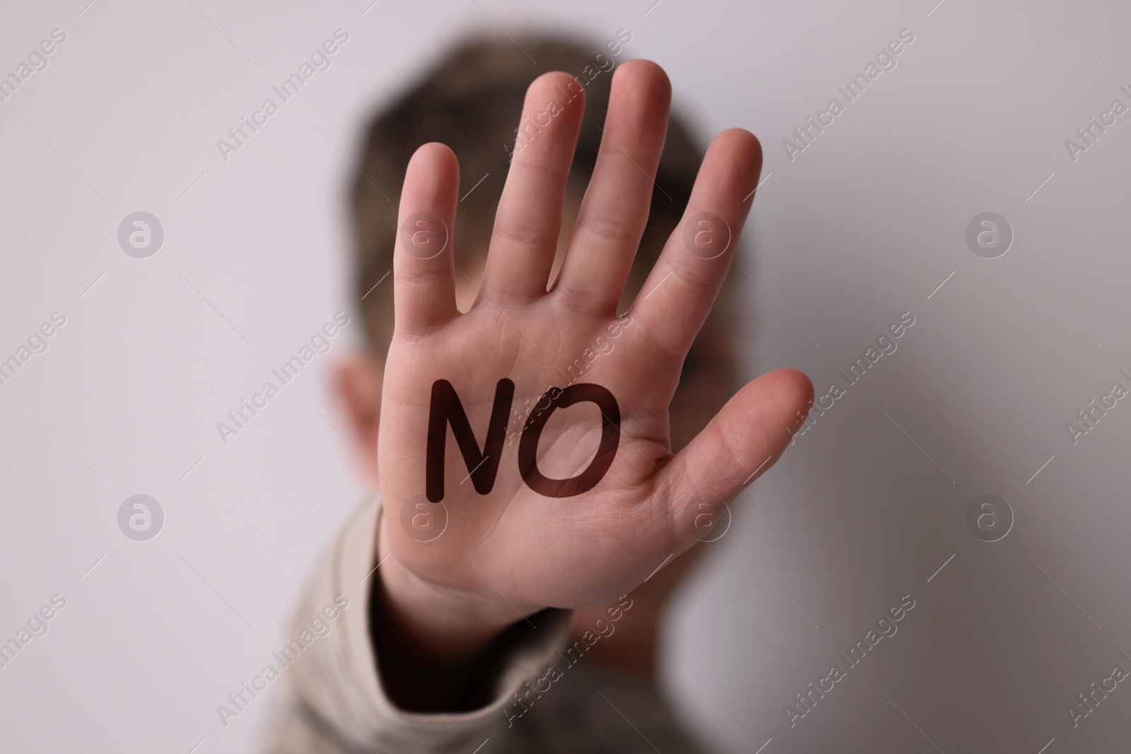 Image of Child abuse. Boy making stop gesture on light background, selective focus. No written on his hand