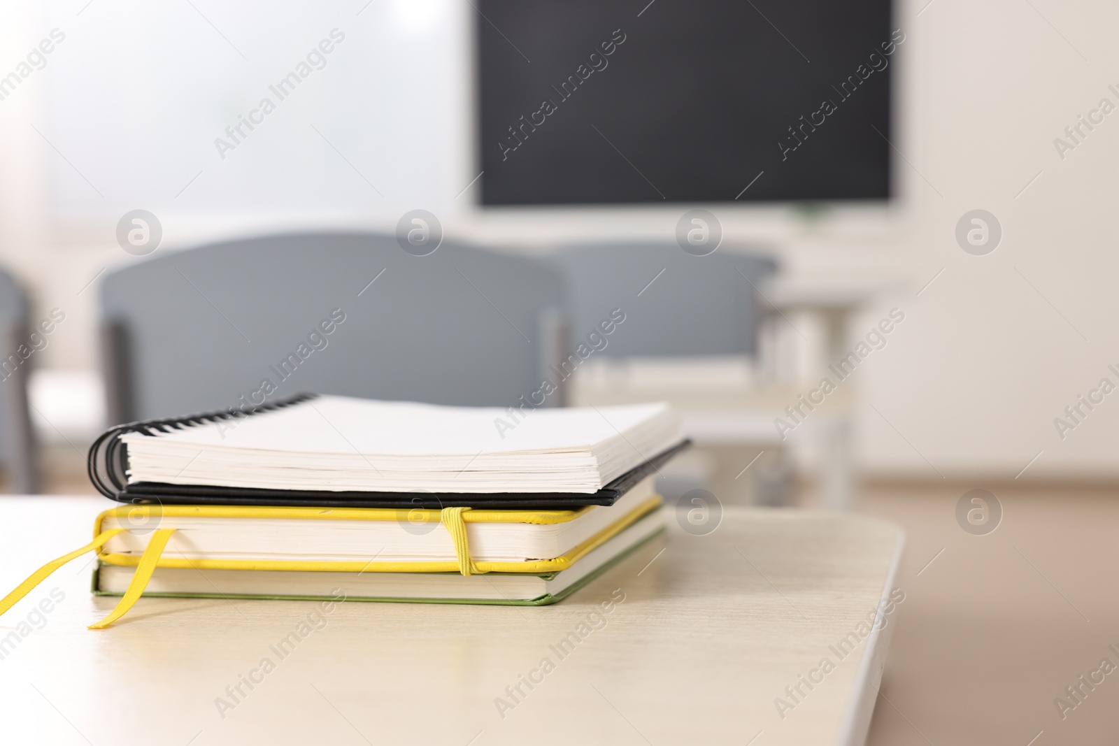 Photo of Stack of notebooks on wooden desk in empty classroom