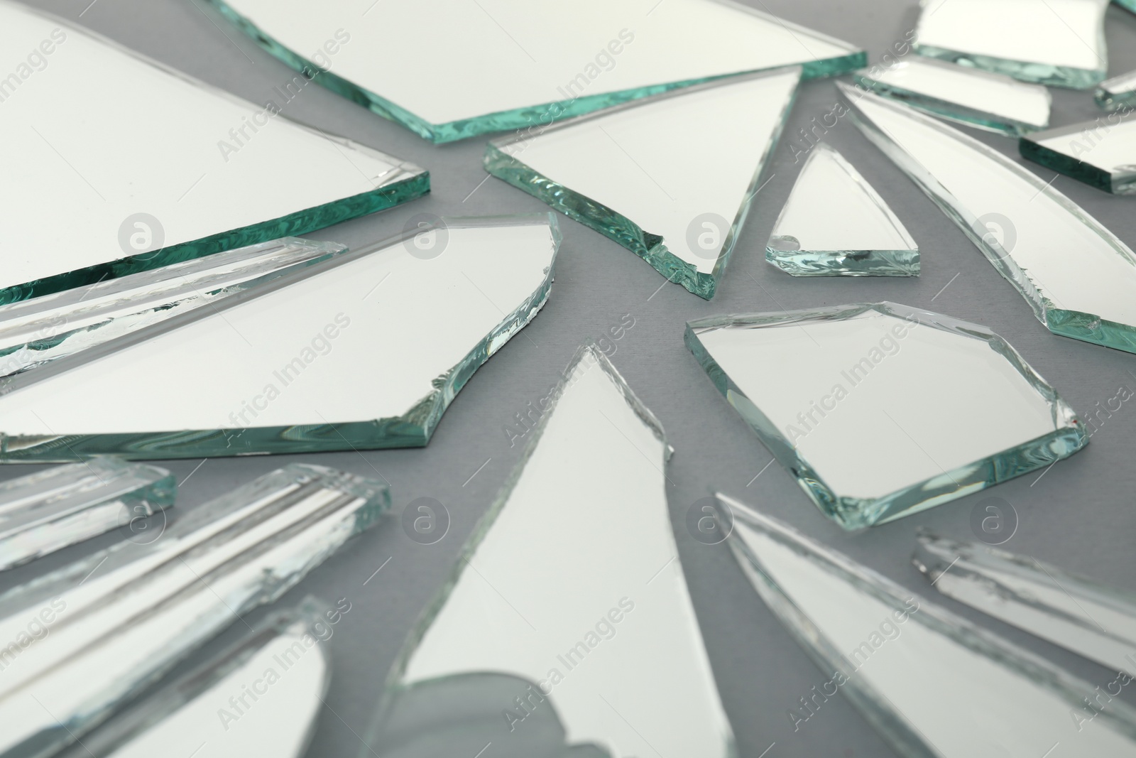 Photo of Shards of broken mirror on grey background, closeup