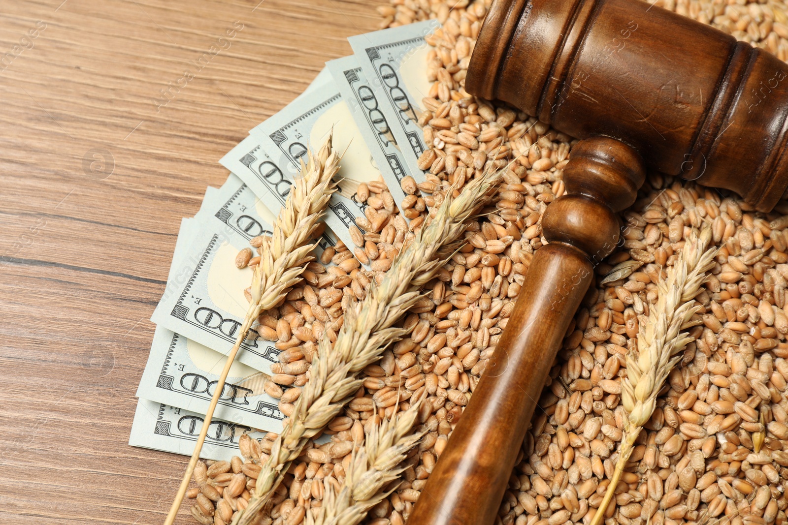 Photo of Dollar banknotes, judge's gavel, wheat ears and grains on wooden table, closeup. Agricultural business