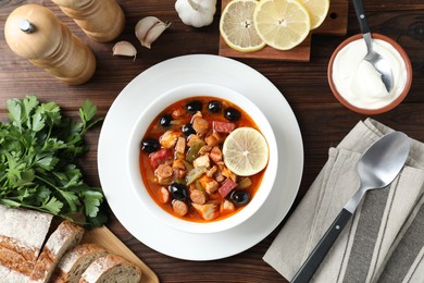 Photo of Meat solyanka soup with sausages, olives and vegetables served on wooden table, flat lay