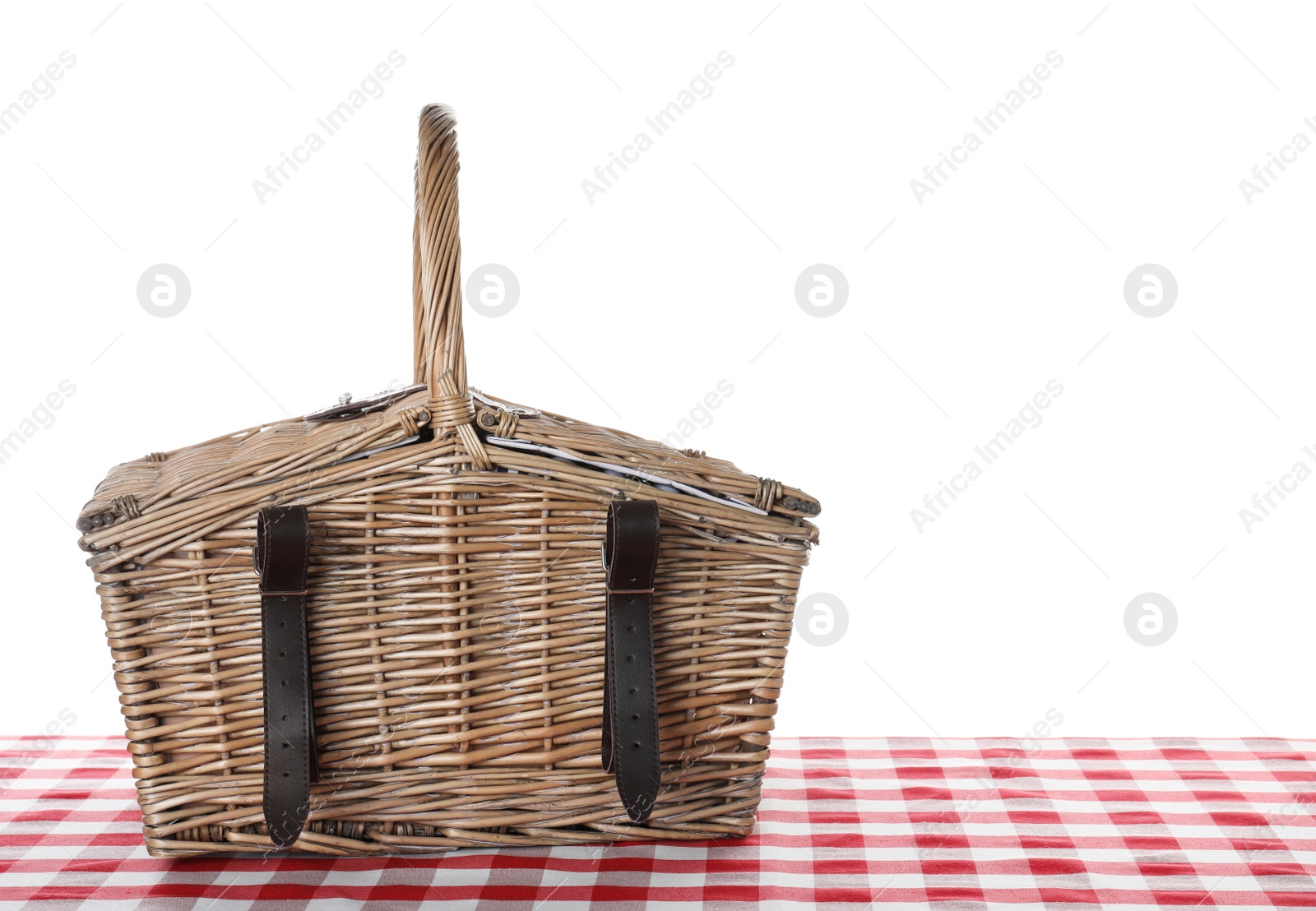 Photo of Closed wicker picnic basket on checkered tablecloth against white background