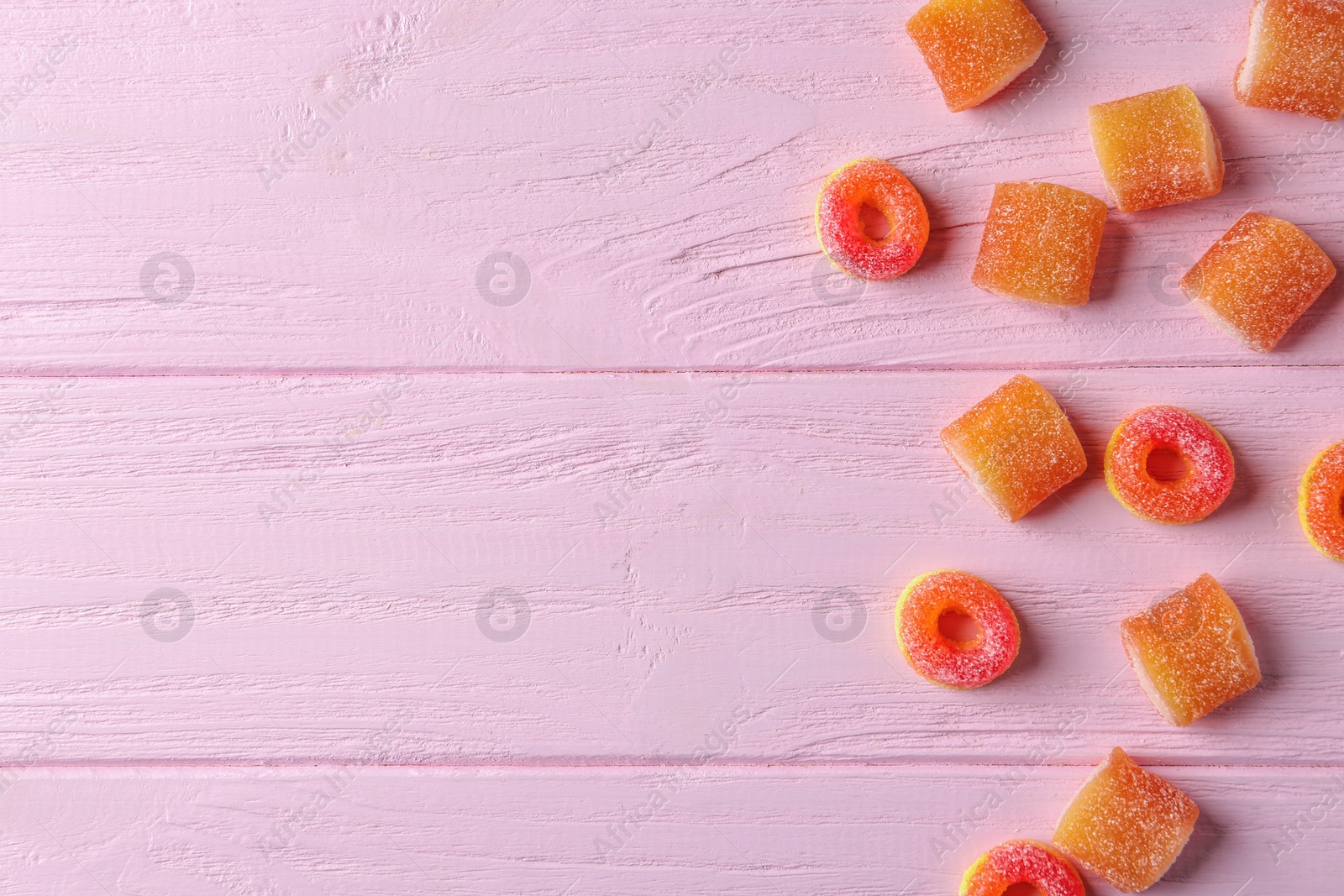 Photo of Tasty jelly candies on pink wooden table, flat lay with space for text