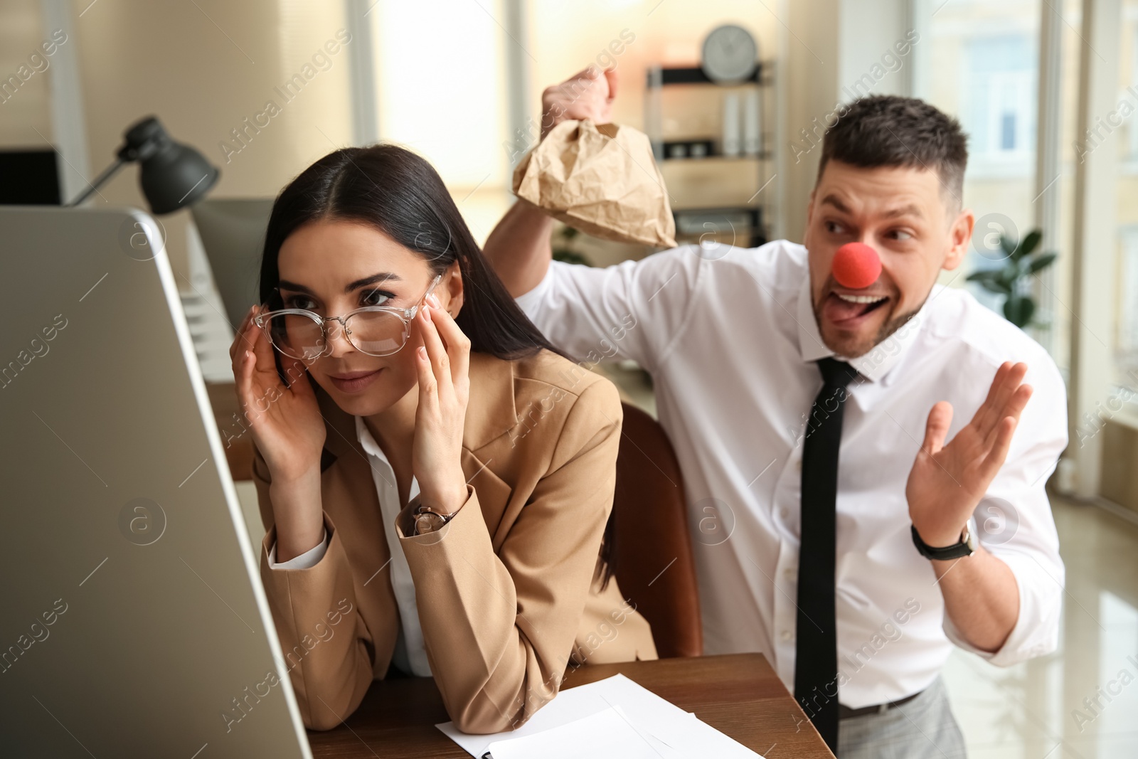 Photo of Man popping paper bag behind his colleague in office. Funny joke