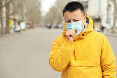 Photo of Asian man wearing medical mask on city street, space for text. Virus outbreak