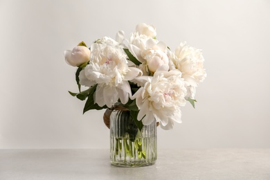 Vase with beautiful blooming peonies on table against light background