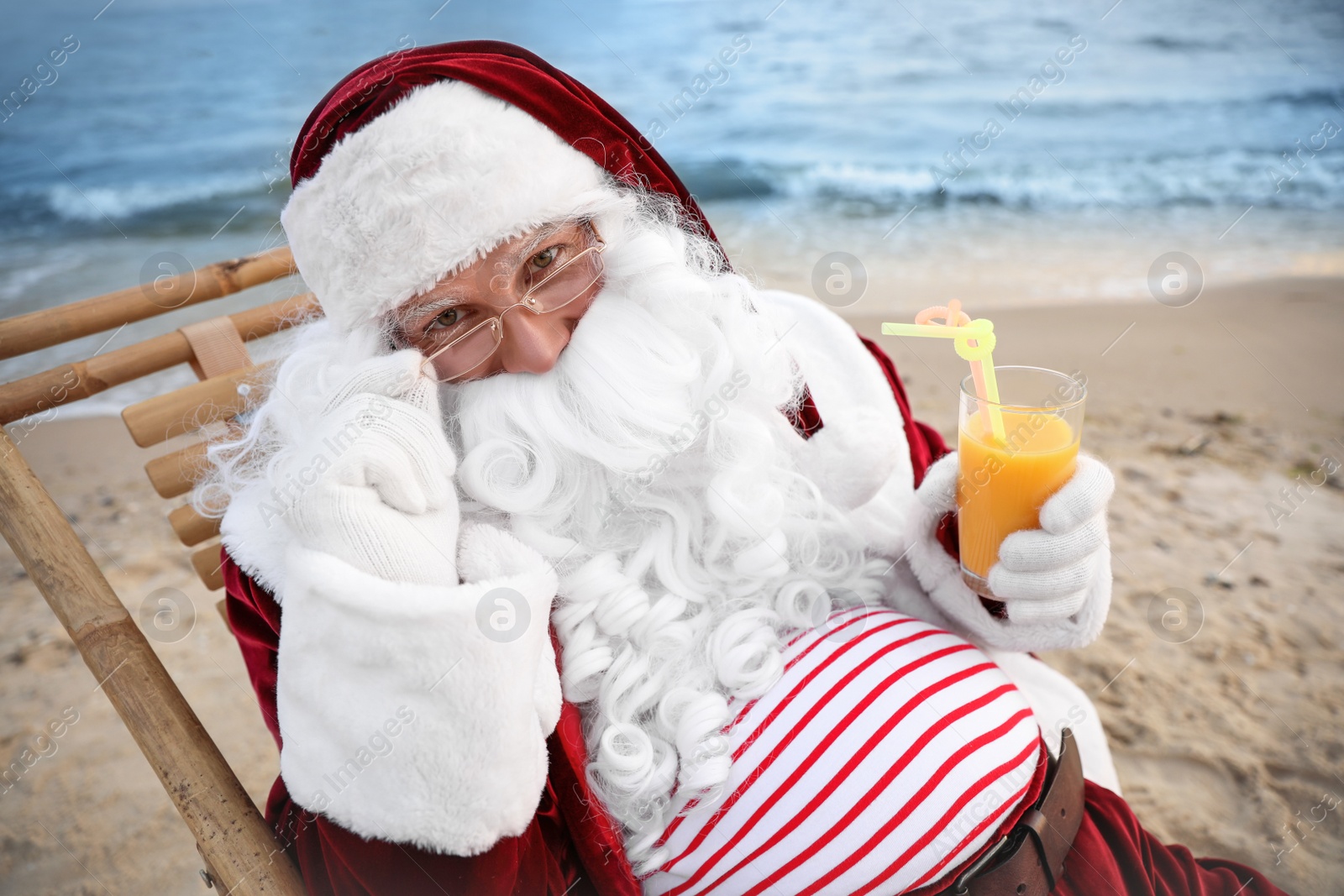 Photo of Santa Claus with cocktail relaxing on beach. Christmas vacation