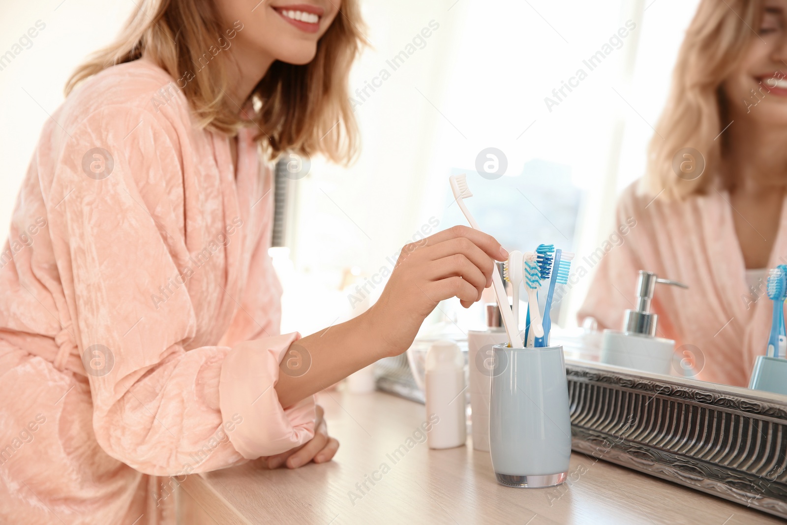 Photo of Young woman taking toothbrush from holder in bathroom. Personal hygiene