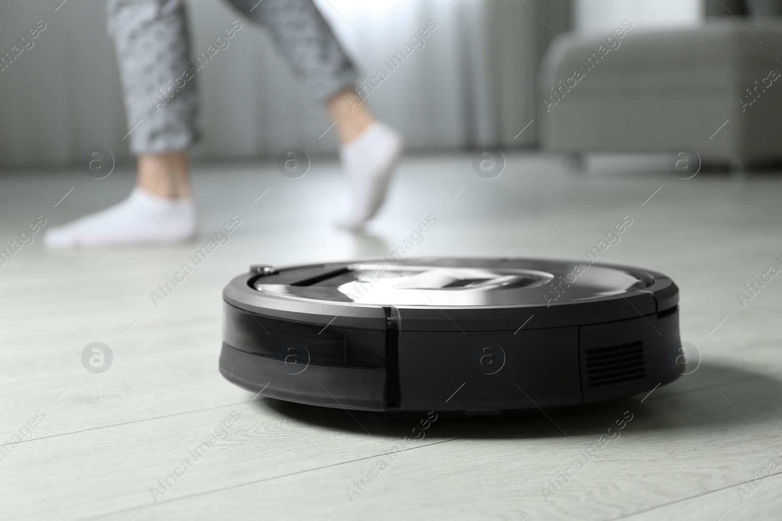 Photo of Modern robotic vacuum cleaner and blurred woman on background