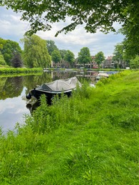 Photo of Beautiful view of city canal with moored boat surrounded by greenery