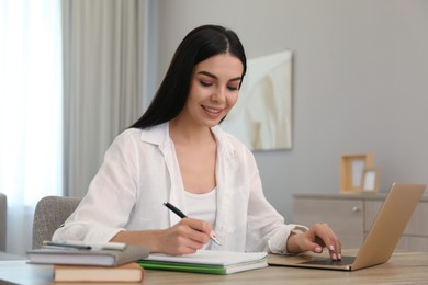 Young woman taking notes during online webinar at table indoors