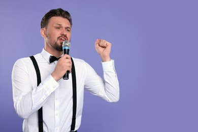 Handsome man with microphone singing on violet background. Space for text