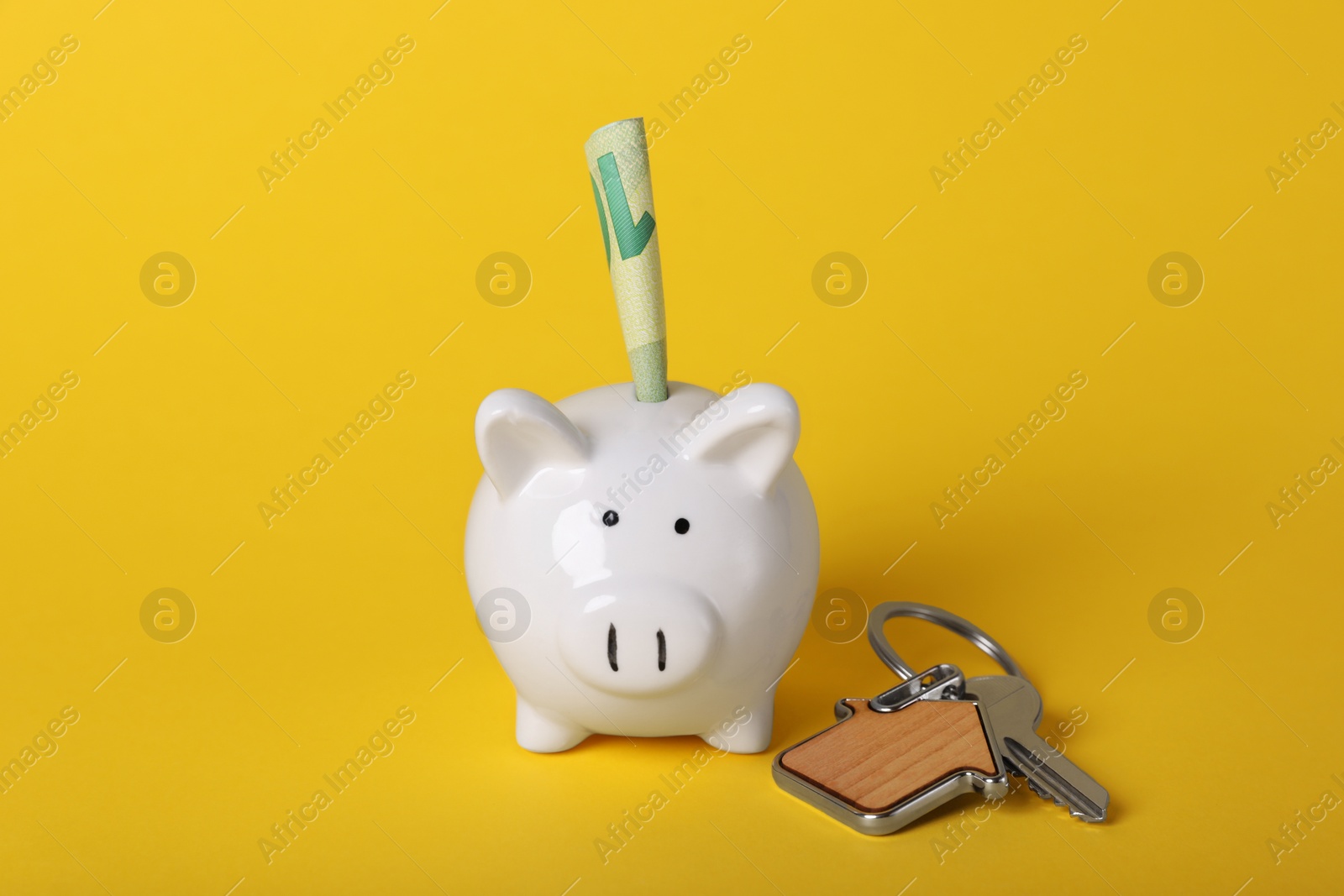 Photo of Ceramic piggy bank, euro banknote and key with trinket on yellow background. Financial savings