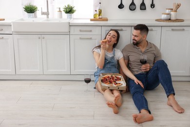 Happy young couple eating pizza in kitchen. Space for text