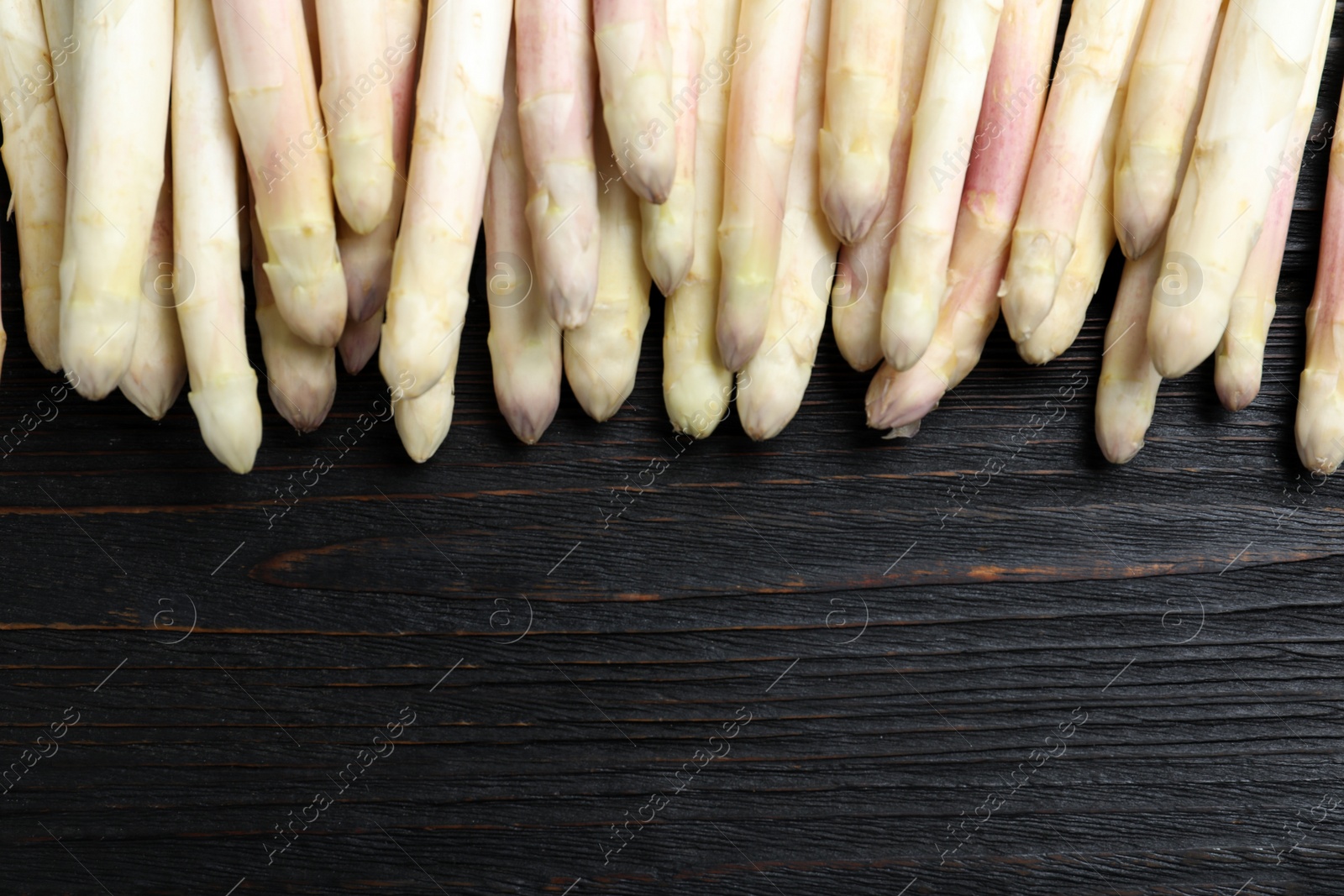 Photo of Fresh white asparagus on black wooden table, flat lay. Space for text