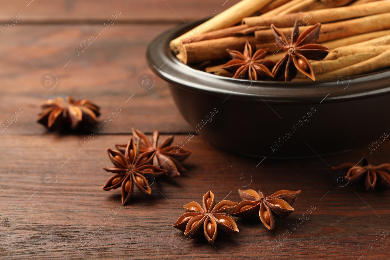 Photo of Bowl with cinnamon sticks and star anise on wooden table, closeup