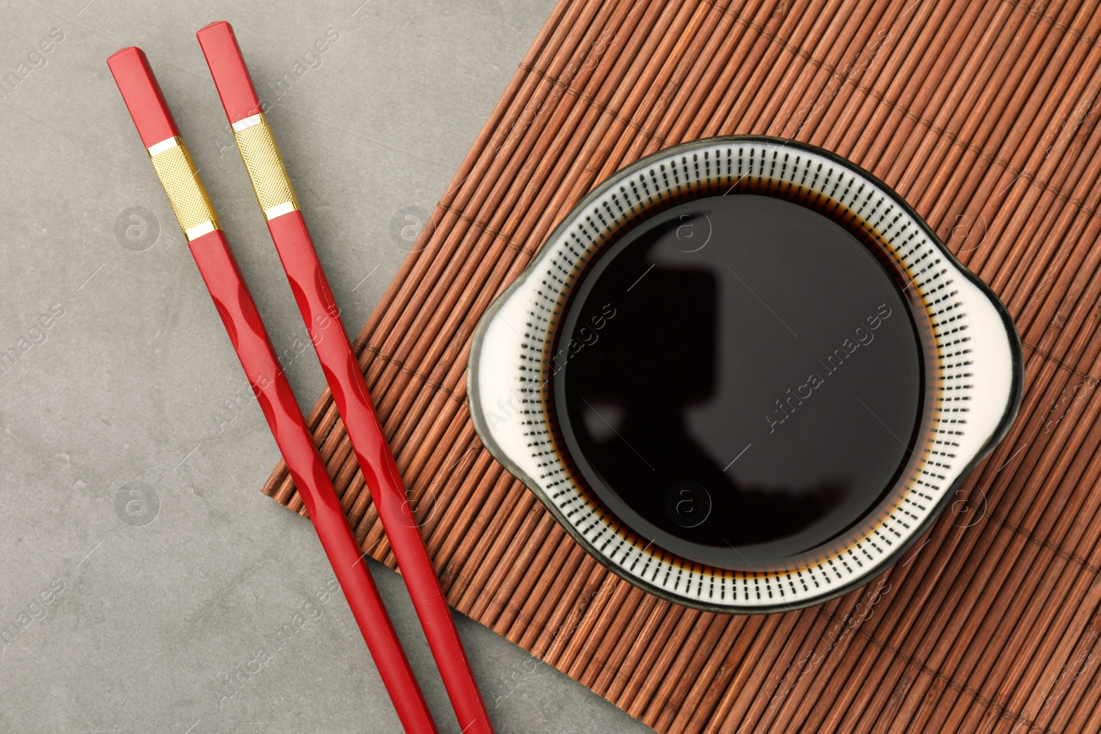 Photo of Bowl of soy sauce and chopsticks on grey table, flat lay