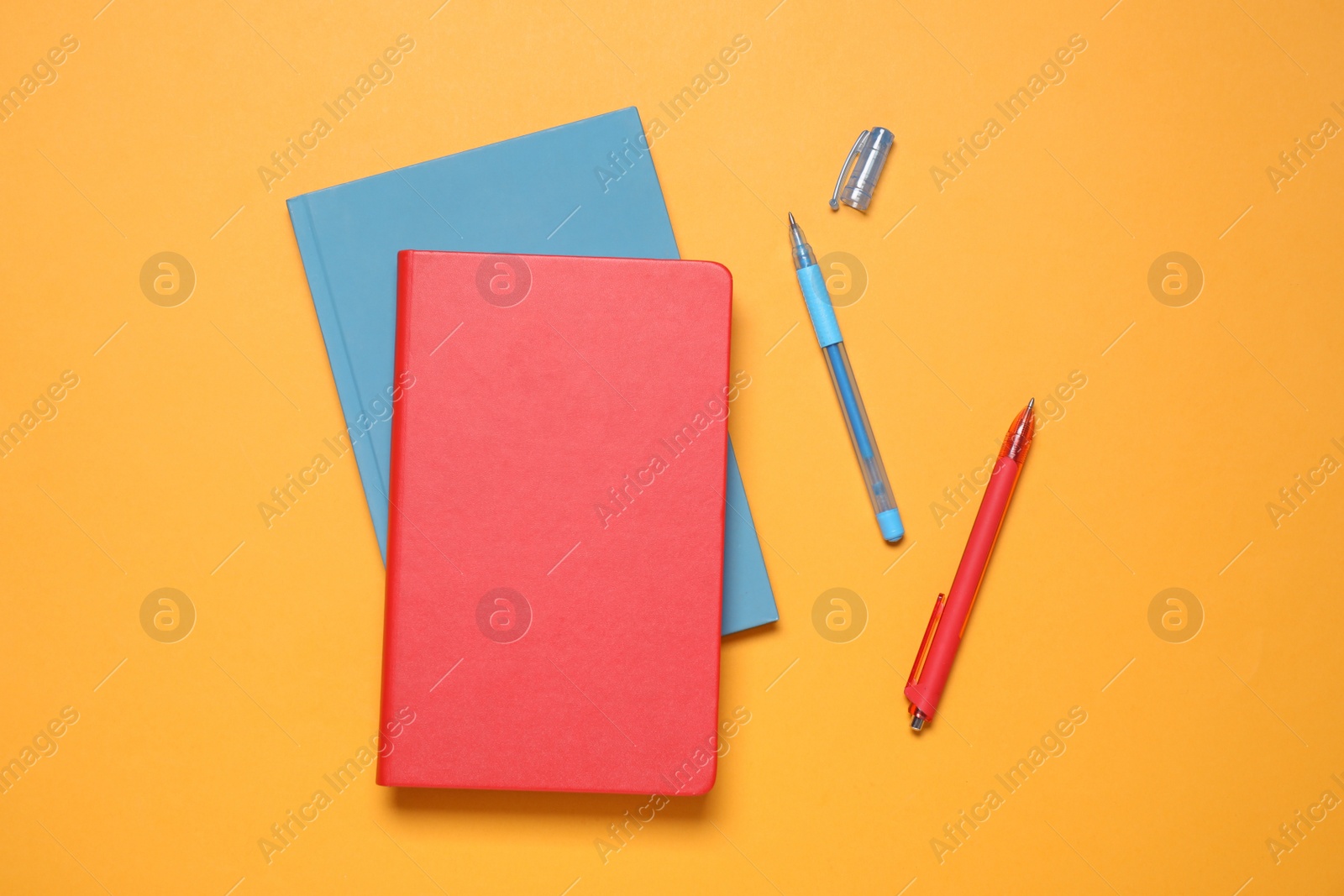 Photo of Stylish notepads and pens on orange background, flat lay