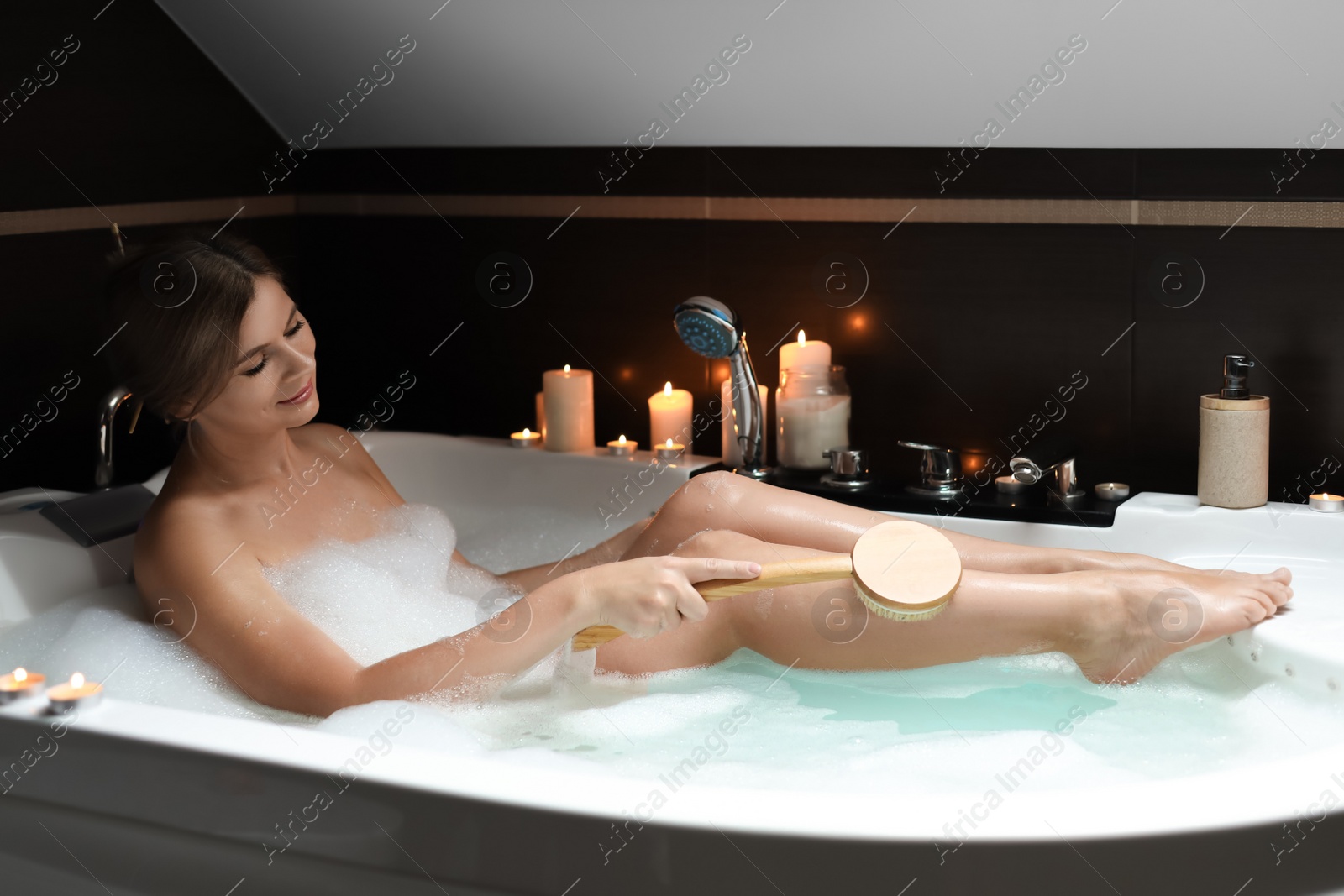 Photo of Beautiful woman rubbing leg with brush while taking bubble bath. Romantic atmosphere