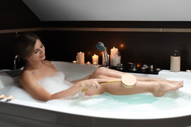 Photo of Beautiful woman rubbing leg with brush while taking bubble bath. Romantic atmosphere