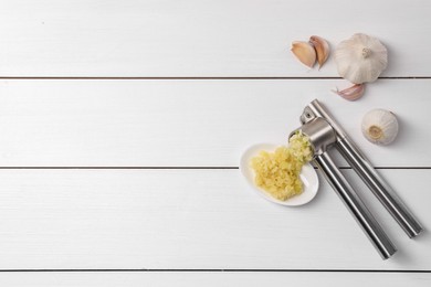 Photo of One metal press and garlic on white wooden table, flat lay. Space for text