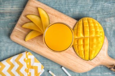 Glass of fresh mango juice and cut fruits on wooden table, top view