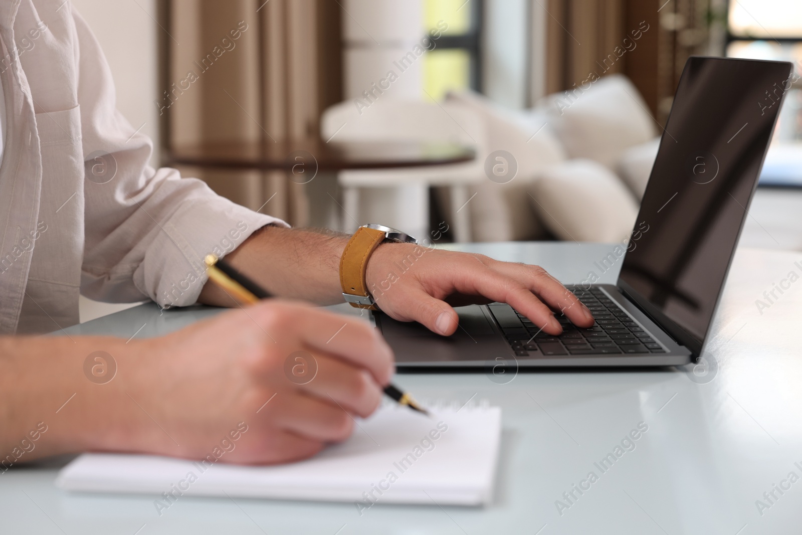 Photo of Man using laptop and writing something at table in cafe, closeup