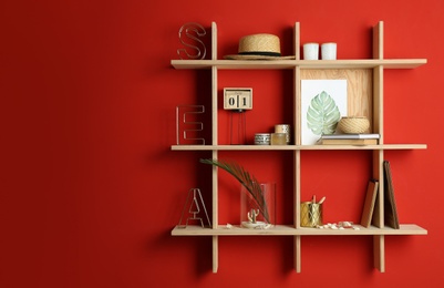 Stylish wooden shelves with decorative elements on red wall. Space for text