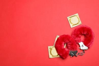 Photo of Furry handcuffs and condoms on red background, top view with space for text. Sex game