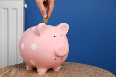 Photo of Woman putting coin into piggy bank near heating radiator, closeup. Space for text