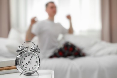Man stretching in bedroom, focus on alarm clock. Space for text