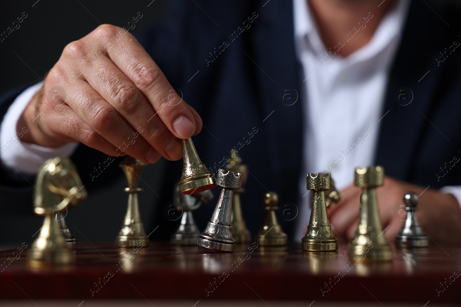 Photo of Man with game piece playing chess at checkerboard against dark background, closeup