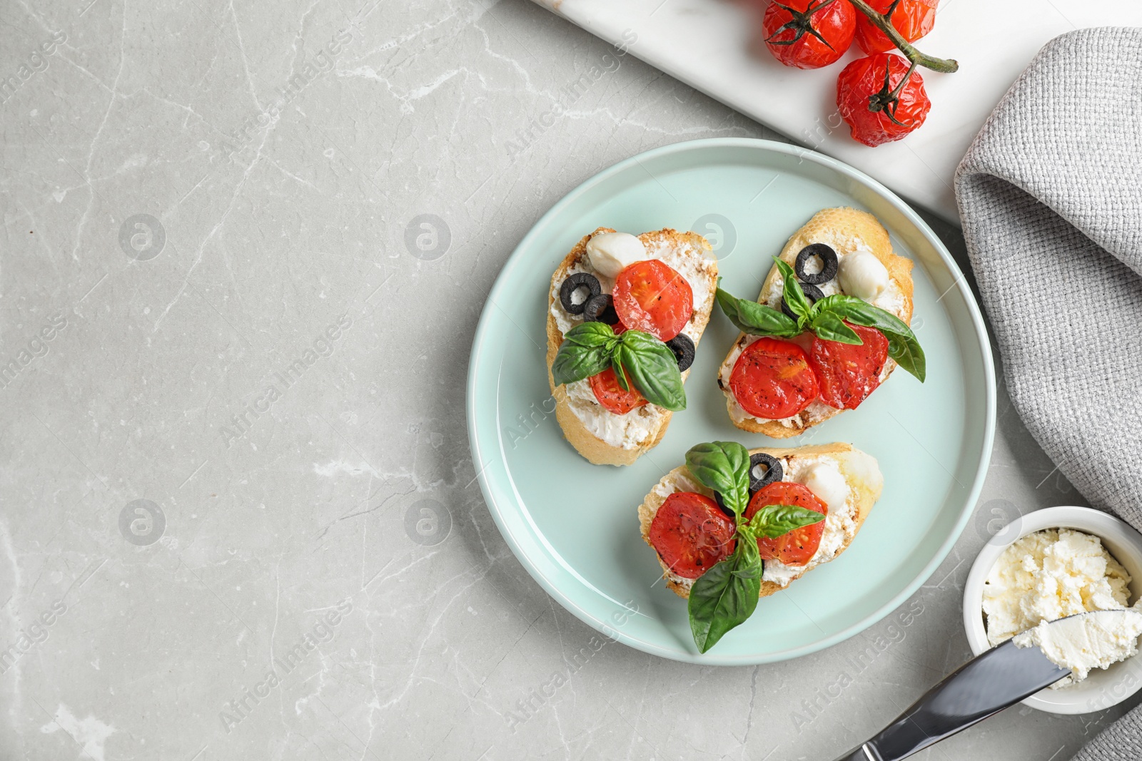 Photo of Plate of delicious tomato bruschettas on light grey marble background, flat lay. Space for text