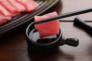 Photo of Dipping tasty sashimi (piece of fresh raw tuna) into soy sauce at wooden table, closeup