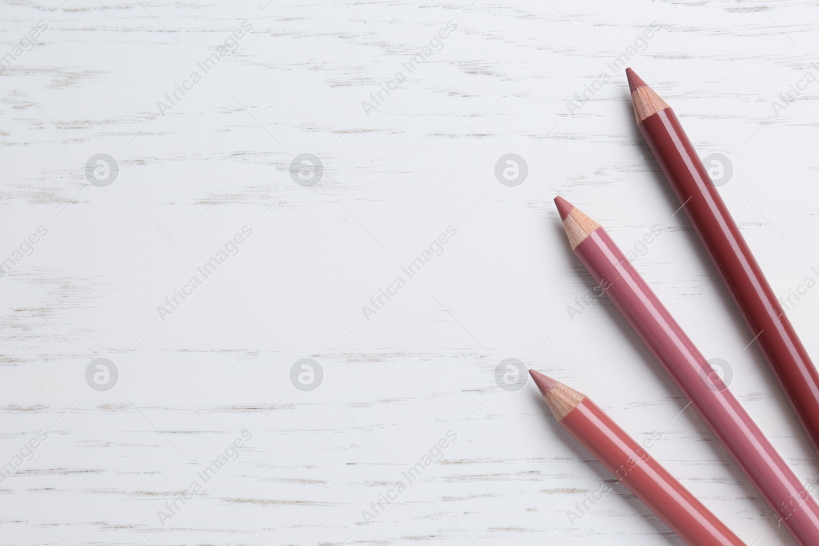 Photo of Different lip pencils on white wooden table, flat lay with space for text. Cosmetic product