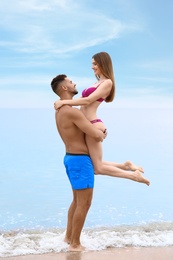 Young man holding his girlfriend in bikini on beach. Lovely couple