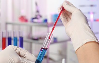 Scientist dripping reagent into test tube with sample in chemistry laboratory, closeup