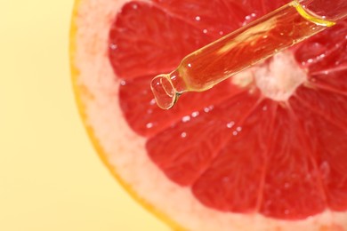 Dripping cosmetic serum from pipette onto grapefruit slice against yellow background, top view